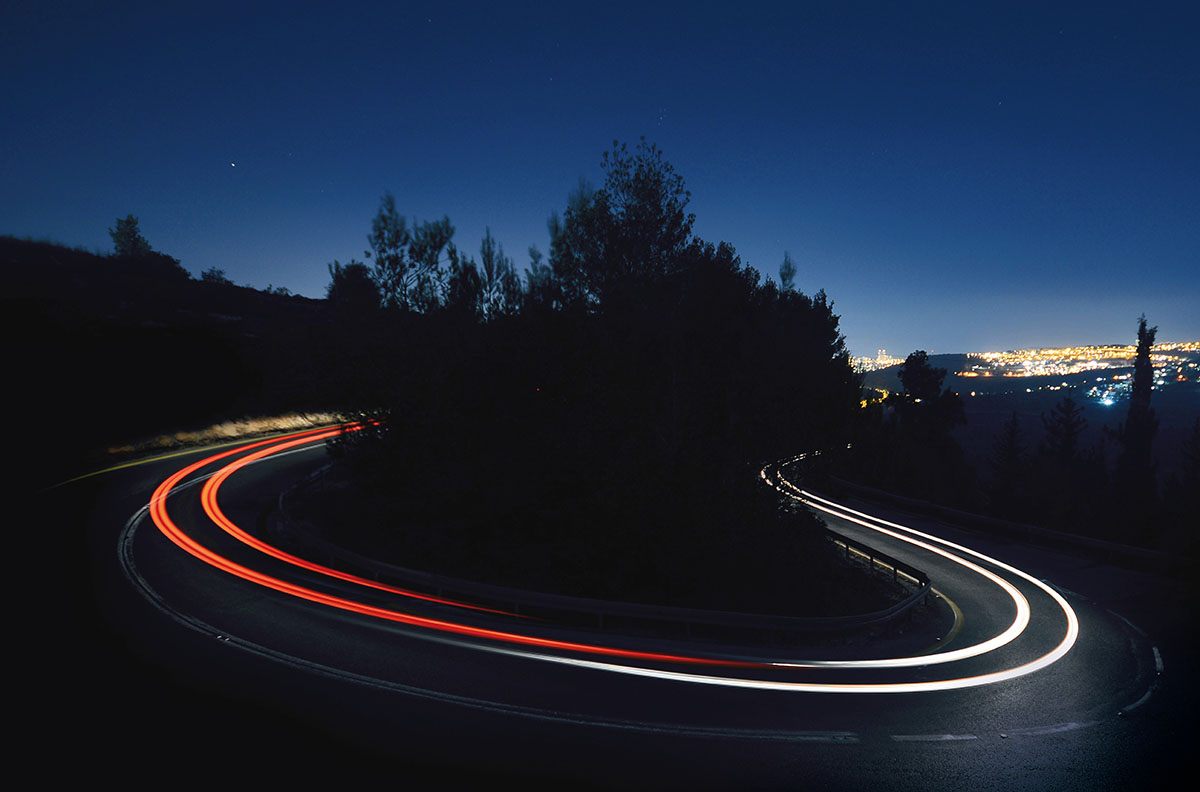 Kehre mit Leuchtspuren von vorbeifahrenden PKW-Rücklichtern in Dämmerung